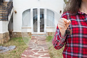 Real estate and property concept - Close up of woman holding house keys on house shaped keychain in front of a new home