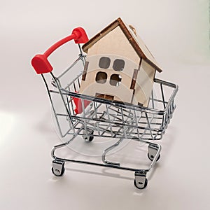 Real estate sales and realtor services. Buying a new home and housing, concept. A small model of a wooden house with a toy shoppin