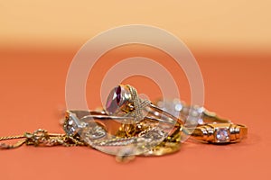 Real gold rings with diamonds, gems, neckless on orange yellow background close up macro shot,