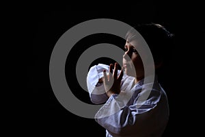 Real karate boy in white kimono isolated on dark background. Child ready for martial arts fight. Kid fighting at judo training.