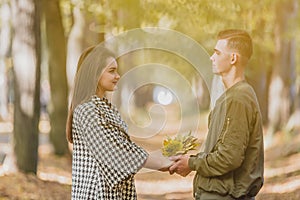 Real love. Beautiful young couple holding a bundle of leaves in hands and keeping eye contact on sunny autumn day in