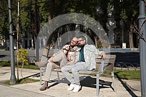 Real marriage of gay couple, holding hands, heads together and eyes closed, sitting on a wooden bench, complicit and happy.