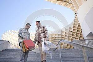 Real marriage of gay couple, holding hands, walking down some stairs and with many shopping bags in the other hand, happy and