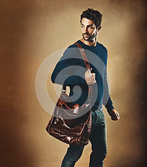 Real men can pull off a bag. Studio shot of a handsome young man carrying a bag against a brown background.