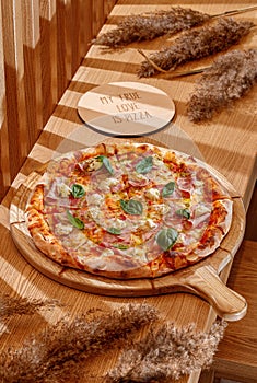 A real neapolitan pizza margherita on a traditional wooden plate. Wooden background, top view