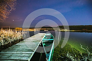 Real Night Sky Stars Above Old Pier With Moored Wooden Fishing Boat. Natural Starry Sky And Countryside Landscape With