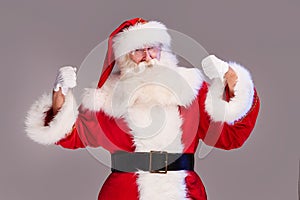 Real old Santa Claus on showing his power, posing on a grey studio background. Merry Christmas and Happy New Year! Copy space