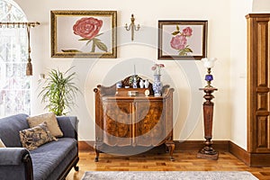 Real photo of an antique cabinet with porcelain decorations, paintings with roses and blue sofa in a living room interior