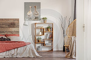 Real photo of a bedroom interior with an oil painting, wooden bookcase and a bed with red and white sheets