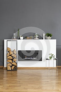 Real photo of a bio fireplace and some wood in dark, simple living room interior