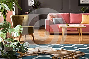 Real photo of blanket placed on moroccan trellis carpet in living room interior with green armchair, powder pink couch with