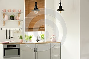 Real photo of a bright kitchen interior with wooden counter, black lamps, white cupboards and pink accents photo