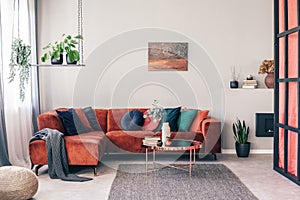 Real photo of colorful pillows on a red corner couch in white living room interior with gray rug