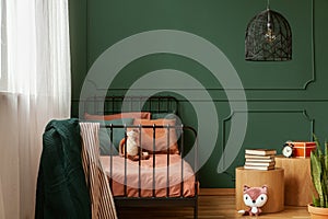 Real photo of a cute, green and orange bedroom interior for a kid with plush fox toys, molding on green wall and books on bedside