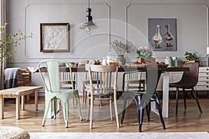 Real photo of an eclectic dining room interior with various chairs at the table, lamp and painting with ducks photo