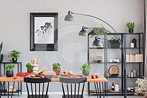 Real photo of an elegant daily room interior with a black shelf, lamp and dining table with herbs, bread and vegetables