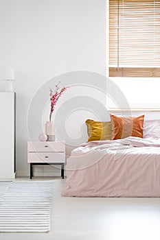 Real photo of a feminine bedroom interior with pink sheets on a