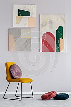 Gray living room interior with a set of modern paintings on the wall and a velvet cushion on a yellow chair photo