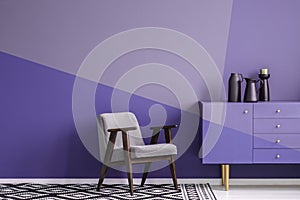 Real photo of a gray, wooden armchair on patterned, black and white rug in creative living room interior with geometric, violet w photo