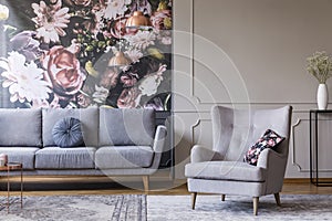 Real photo of a grey living room interior with a sofa, armchair, wallpaper and wall molding