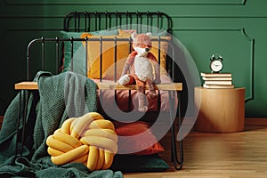 Real photo of a knot pillow, green blanket and plush fox on a wooden bench in front of a black bed in cute bedroom interior