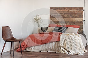 Real photo of a leather chair in a natural bedroom interior with a wooden bed, white walls and string of lights