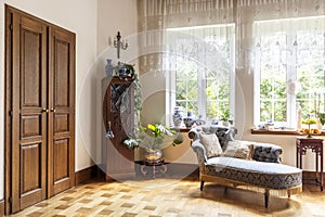 Real photo of a living room interior with a chaise longue, porcelain vases, wooden door and windows with curtains photo