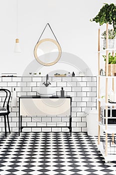 Real photo of a modern bathroom interior with checkered floor, mirror, wash basin with a cupboard and plants