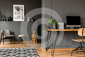 Real photo of open space home interior of a freelancer with simple workspace at the front and a living room with gray armchair in