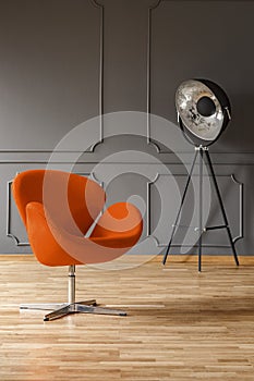 Real photo of orange armchair and big metal studio lamp standing