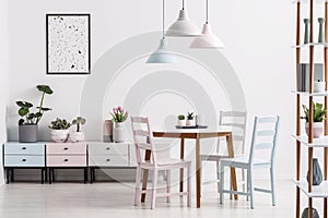 Real photo of a pastel dining room interior with a table, chairs