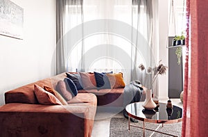 Real photo of pillows on a red corner sofa standing near the window with gray drapes in living room interior