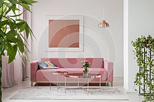 Real photo of a pink couch, round coffee tables and painting in a modern living room interior photo