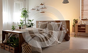 Real photo of a romantic bedroom interior with a double bed with sheets, plants and wooden shelves
