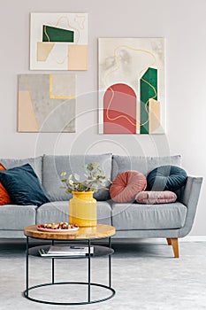 Real photo of a round coffee table with walnuts and yellow vase standing in front of a gray settee in a living room interior