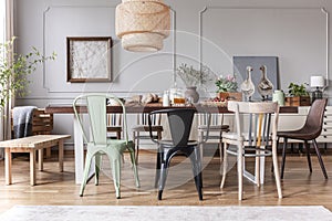 Real photo of a rustical dining room interior with a wicker lamp, table, chairs and plants photo