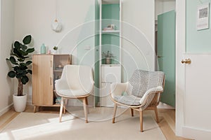 Real photo of a spacious, pastel office interior with mint cupboard standing against white wall with copy space next to an armchai