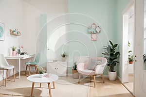 Real photo of a spacious, pastel office interior with mint cupboard standing against white wall with copy space next to an armchai