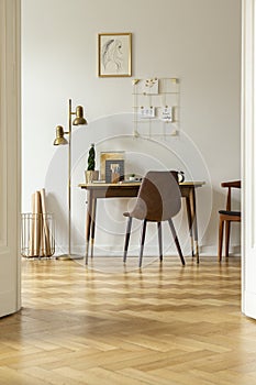 Real photo of a vintage home office interior with a desk, chair, lamp and wooden floor