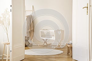 Real photo of white cradle with heart standing in Scandi kid room interior with teddy bear, herringbone parquet and empty wall