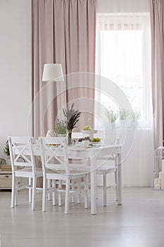 Real photo of white dining room interior with window with curtains, table with fresh lavender and food and lamp