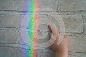 A real rainbow on the wall of brick wallpaper. Child`s hand wants to touch rainbow light reflection