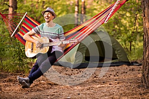 Real relaxation. Handsome young man in hat play guitar while lying in hammock