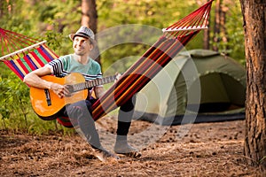 Real relaxation. Handsome young man in hat play guitar while lying in hammock