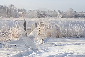 Real Russian Winter. Winter Landscape With Trail Across The Dangerous Rural Suspension Bridge Over The Snowy Foggy River