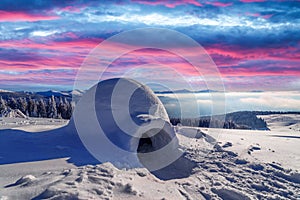 Real snow igloo house in the winter mountains glowing by evening sunlight