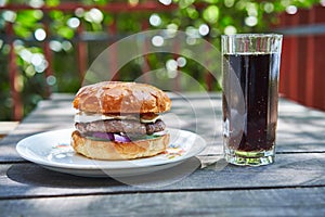 Real tasty and juicy grilled hamburger or cheeseburger served on the white plate with cola drink.