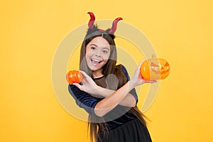 A real treat. halloween devil girl. happy childhood. teenage child in imp horns. cheerful kid hold creepy pumpkin