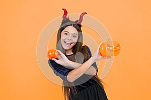 a real treat. halloween devil girl. happy childhood. teenage child in imp horns. cheerful kid hold creepy pumpkin