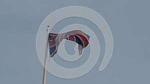 Real Union Jack flag of the United Kingdom on flagpole fluttering in the wind